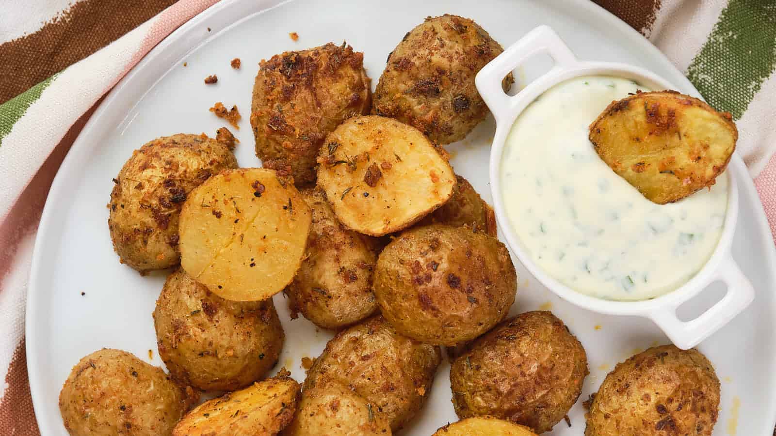 A plate of parmesan potatoes is served with a small ramekin filled with creamy dipping sauce.