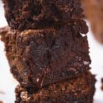 Close-up of a stack of three pumpkin brownies with a rich, moist texture and chunks of melted chocolate.