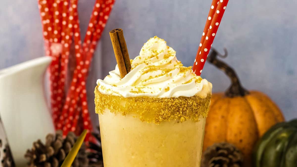 A milkshake in a glass rimmed with sugar, topped with whipped cream and a cinnamon stick,.