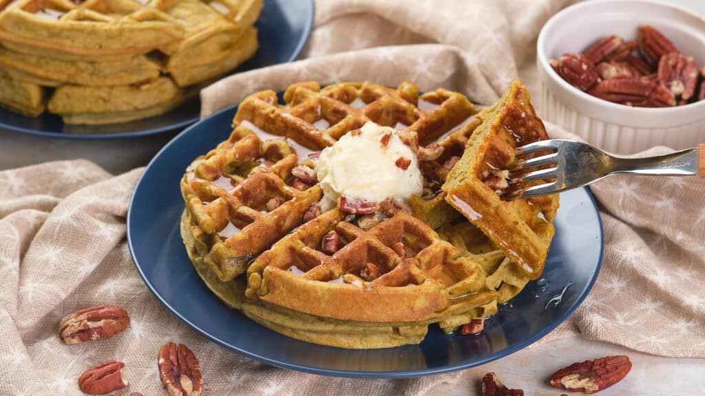 A plate of pumpkin pecan waffles topped with a scoop of butter and syrup.