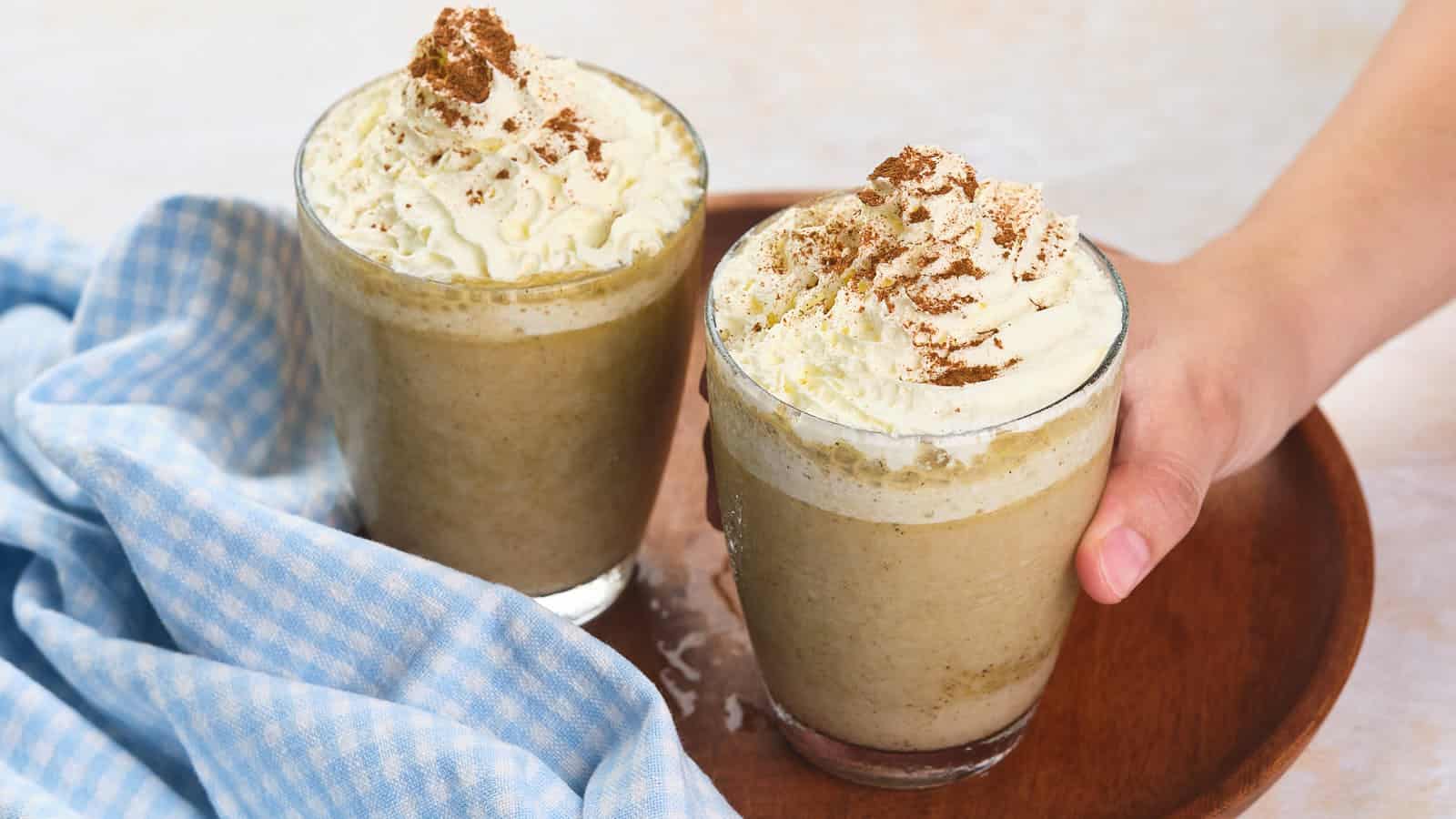 Two glasses of pumpkin spice frappuccino are served on a wooden tray.