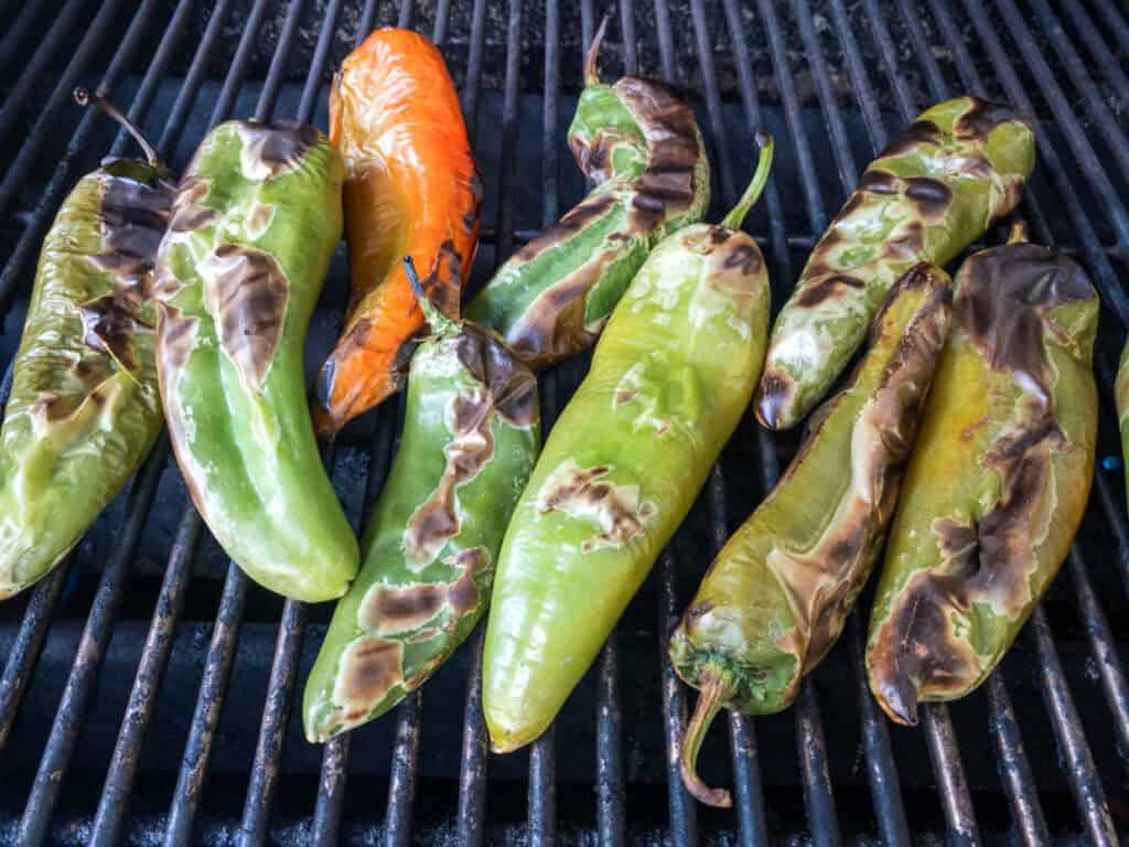 Hatch chile peppers being roasted on a grill, with char marks visible on their skins.