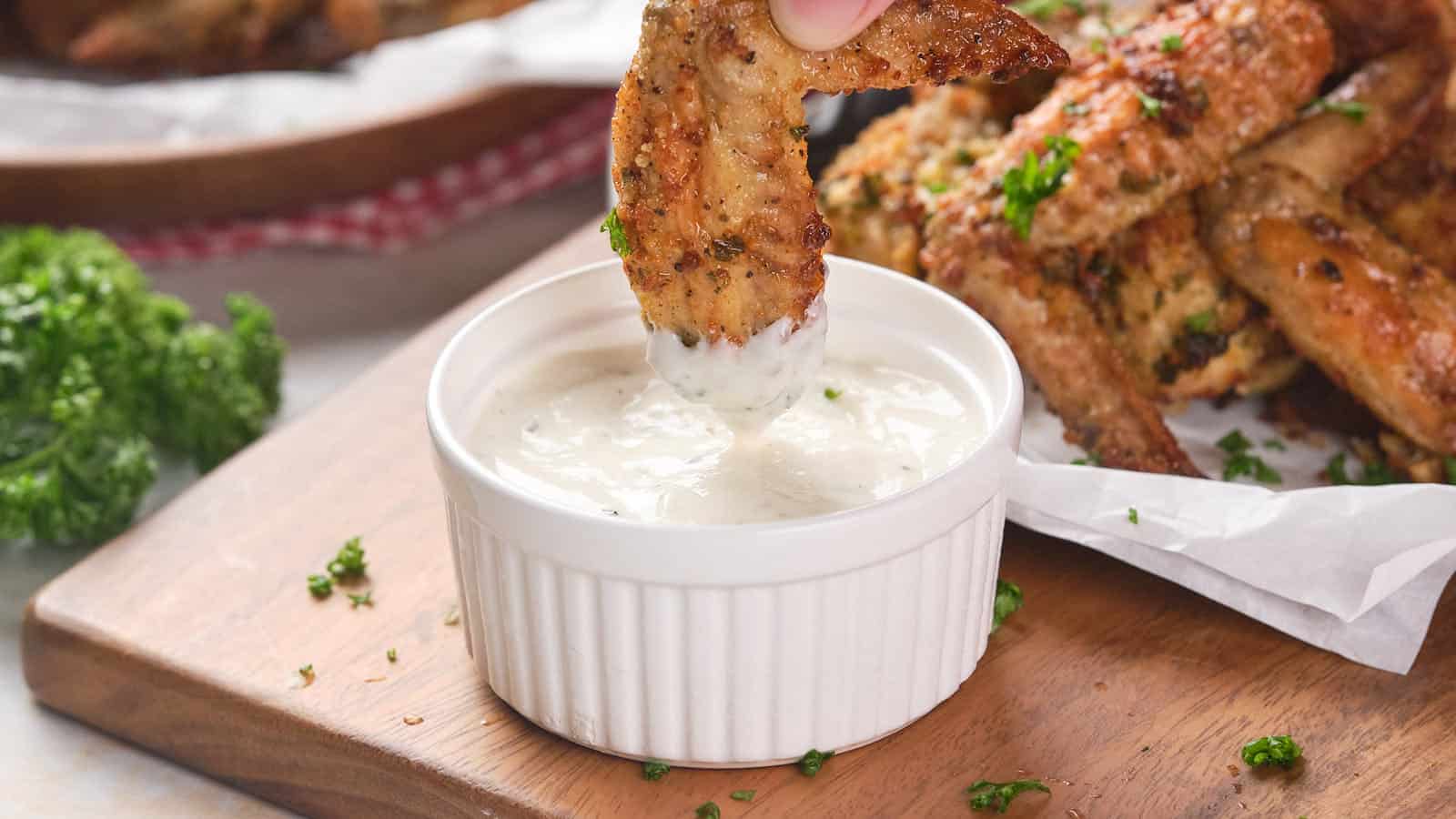 A seasoned chicken wing being dipped into wingstop ranch-dressing in a small ramekin.