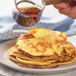 A stack of pancakes topped with butter is being drizzled with syrup.