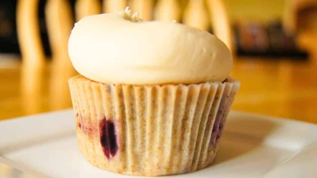 A cherrry cupcake with cream frosting on a white plate.