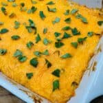 A baked casserole topped with melted cheese and garnished with fresh cilantro in a white rectangular dish.