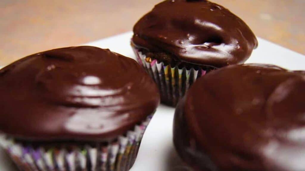 Three chocolate frosted cupcakes on a white plate.