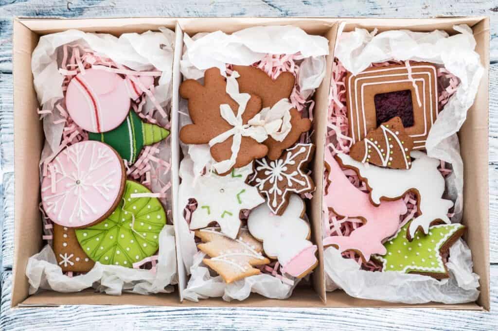 Three sections of assorted decorated cookies in a box with tissue paper, perfect for a holiday cookie exchange. Featuring Christmas-themed shapes and colorful icing, these festive treats are sure to delight.