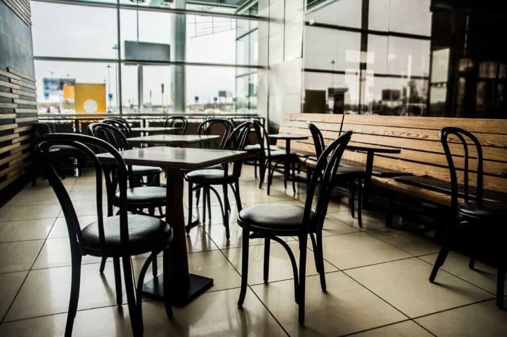 Empty cafe interior with dark wooden chairs and tables, tiled floor, and large windows.