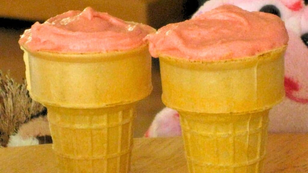 Two ice cream cones with pink ice cream on a wooden surface.