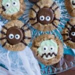 Cookies decorated with cartoonish monster and spider faces, featuring chocolate and icing details, arranged on a glass plate.