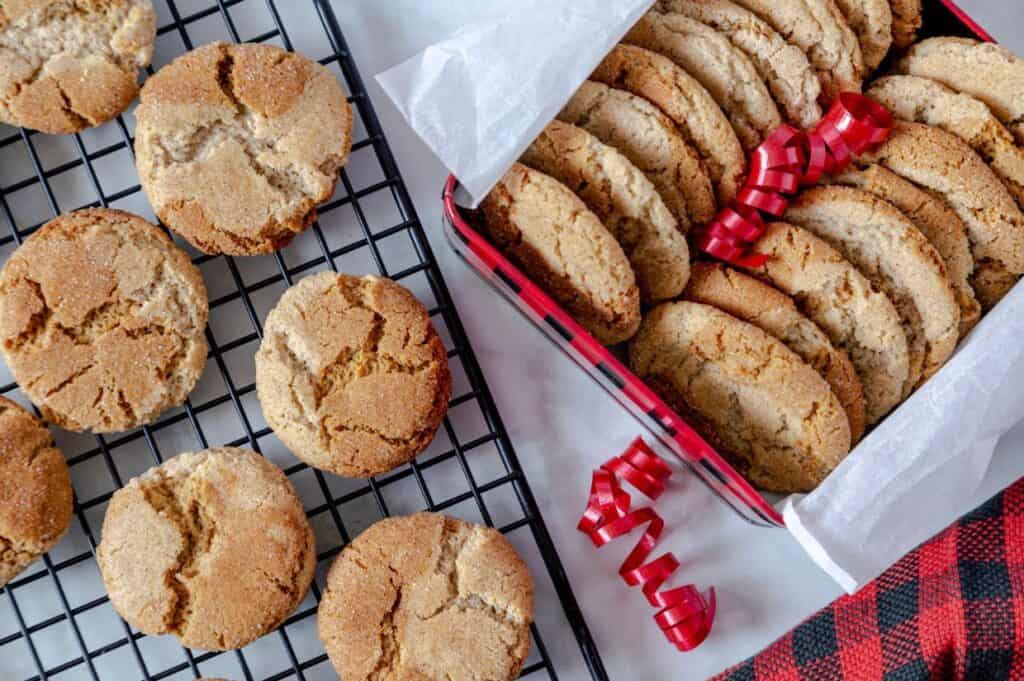 Cookies on a cooling rack and in a lined box with red ribbon decoration, viewed from above, ready for a festive holiday cookie exchange.