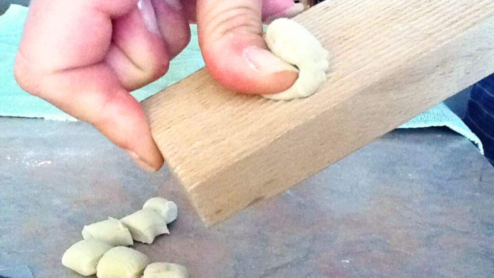 A hand shapes gnocchi dough pieces against a ridged wooden board.