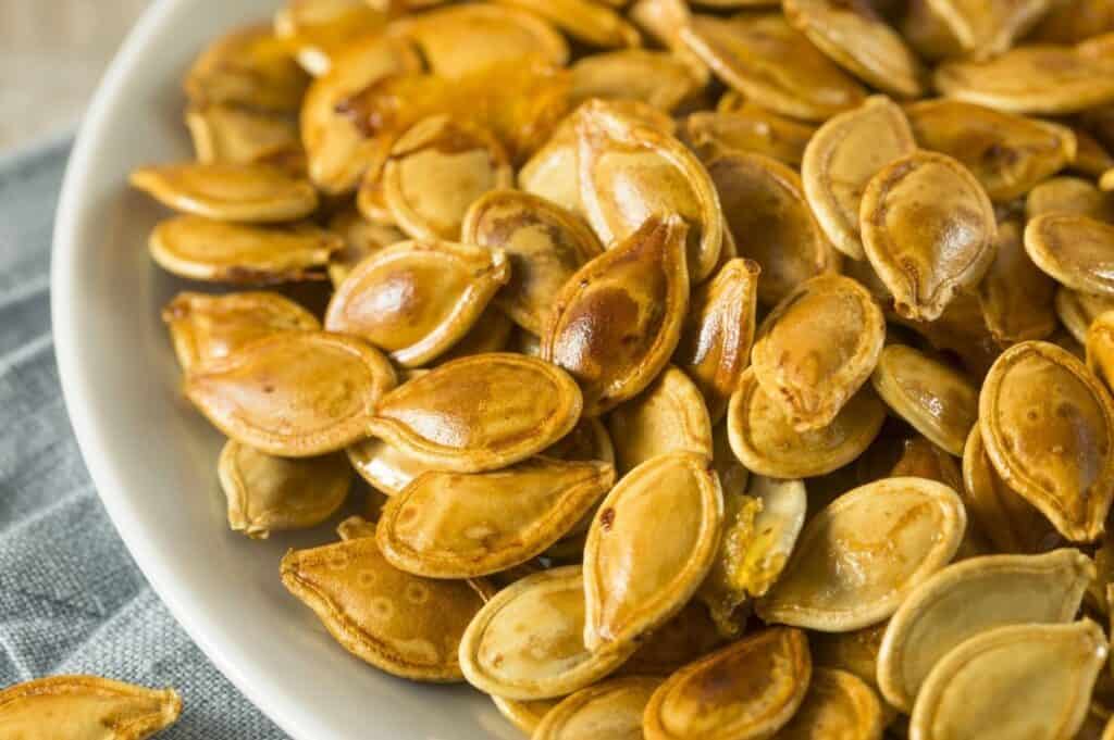 A bowl filled with roasted pumpkin seeds on a cloth surface.