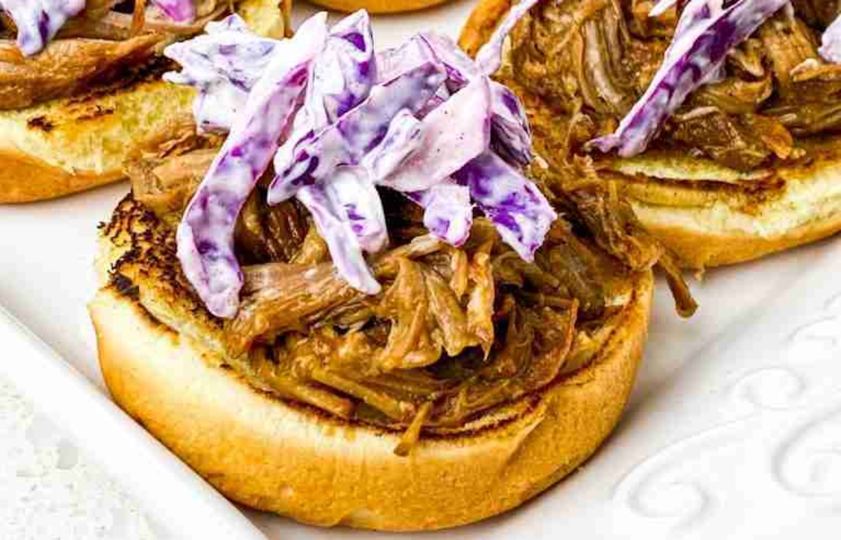 Open-faced sandwich with pulled pork and purple coleslaw on a toasted bun.