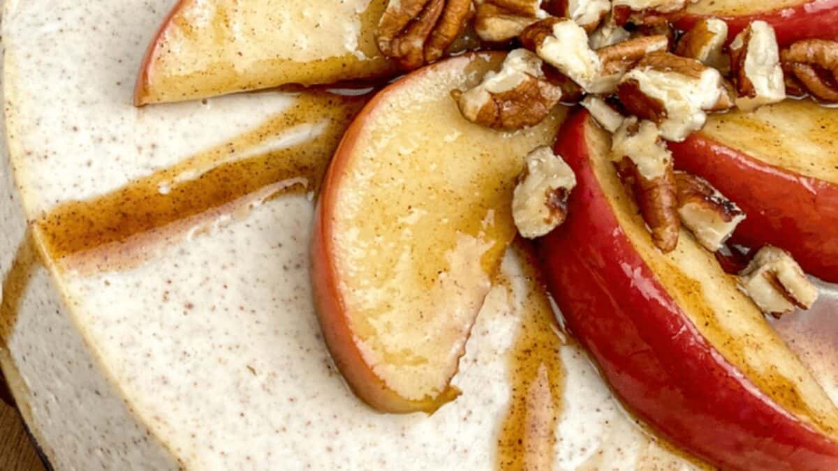 A close-up of a dessert topped with apple slices, chopped pecans, and caramel sauce.