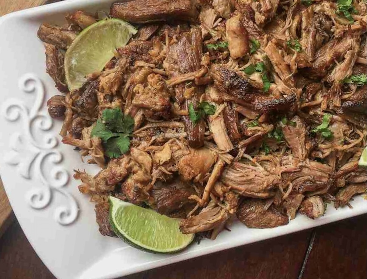 A plate of pulled pork carnitas garnished with lime wedges and cilantro.