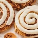 Cinnamon rolls with white icing on top of a parchment paper, with a small pile of cinnamon powder nearby.