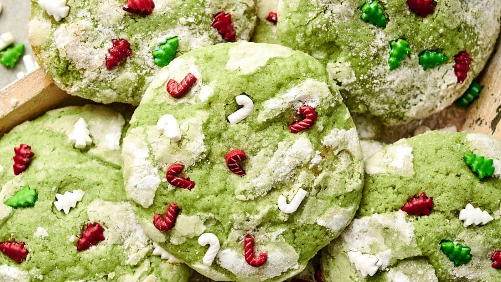 Green cookies topped with powdered sugar and red, green, and white candy shapes resembling trees and candy canes.