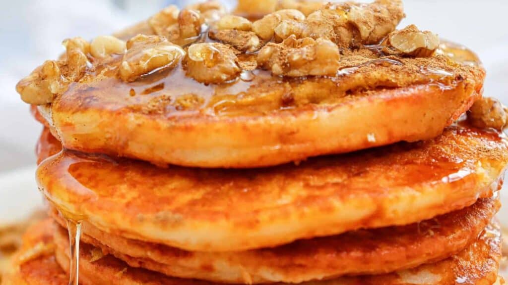 A stack of pancakes topped with walnuts and drizzled with syrup.