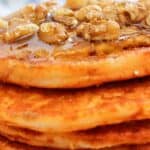 A stack of pancakes topped with walnuts and drizzled with syrup.