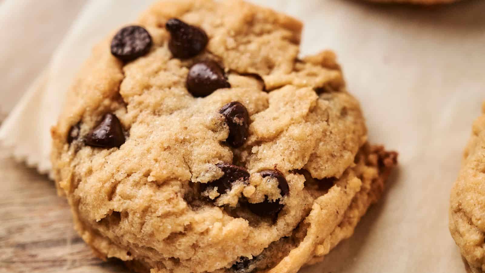 A close-up of a vegan chocolate chip cookie on a piece of parchment paper, showcasing its delightful texture and rich chocolate chips.
