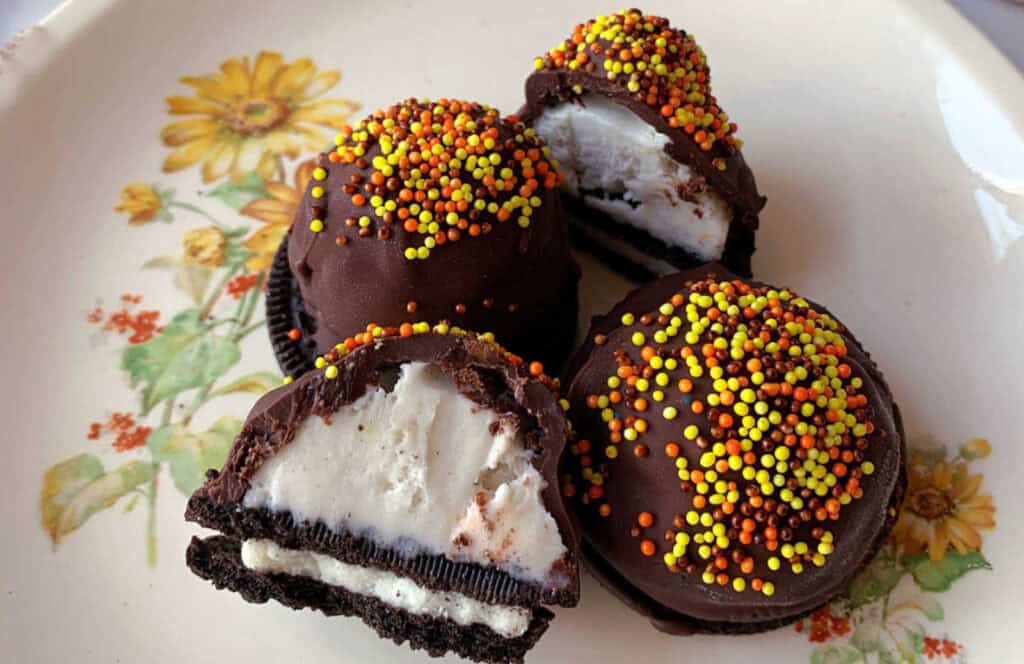 Chocolate-covered ice cream sandwiches topped with orange and yellow sprinkles on a floral-patterned plate.