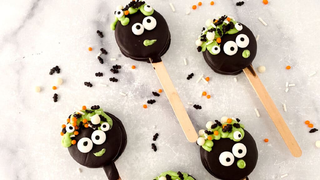 Halloween-themed cake pops with googly eyes and colorful sprinkles on a marble surface.