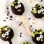 Halloween-themed cake pops with googly eyes and colorful sprinkles on a marble surface.