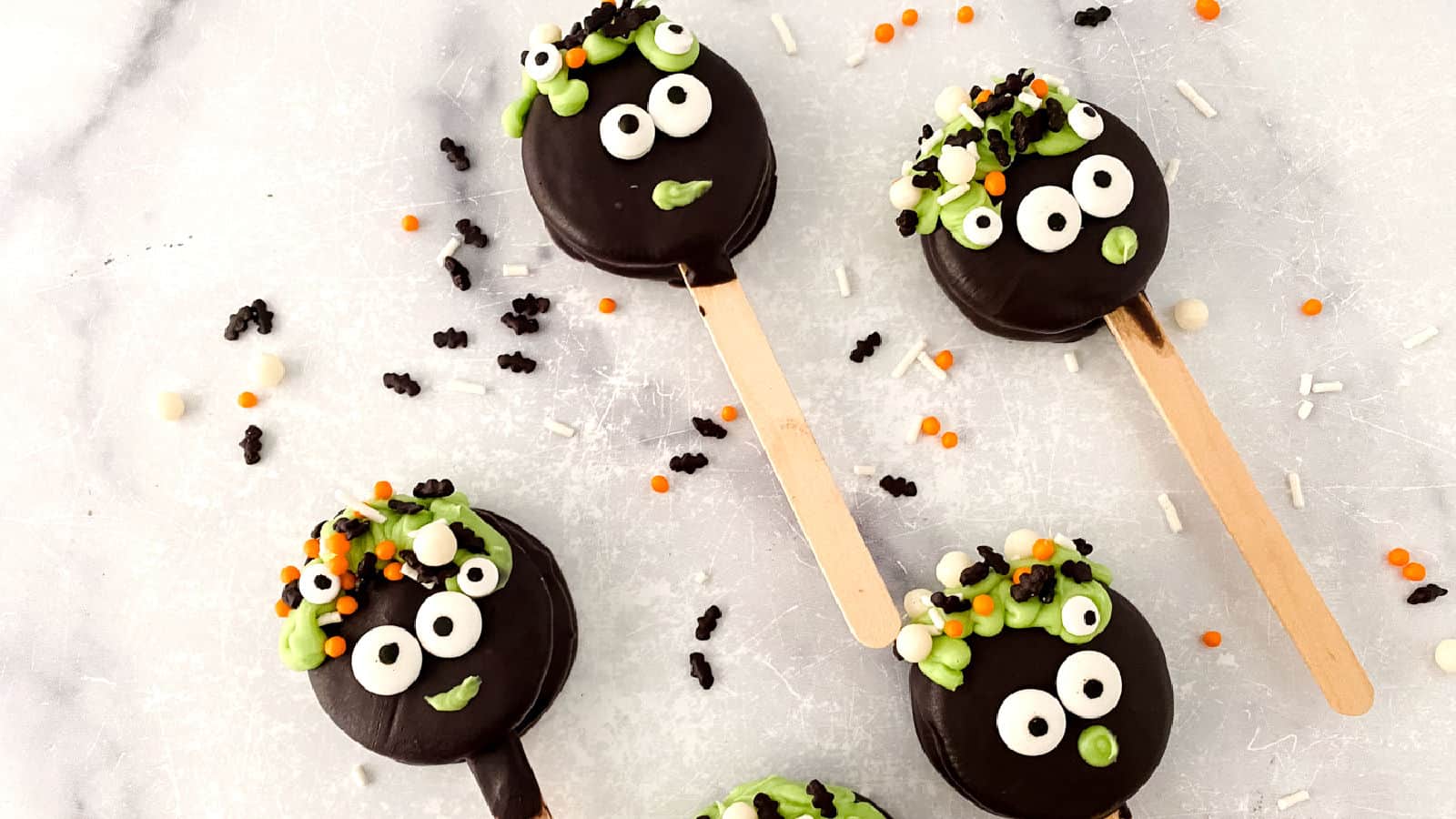 Halloween-themed cake pops with googly eyes and colorful sprinkles on a marble surface.