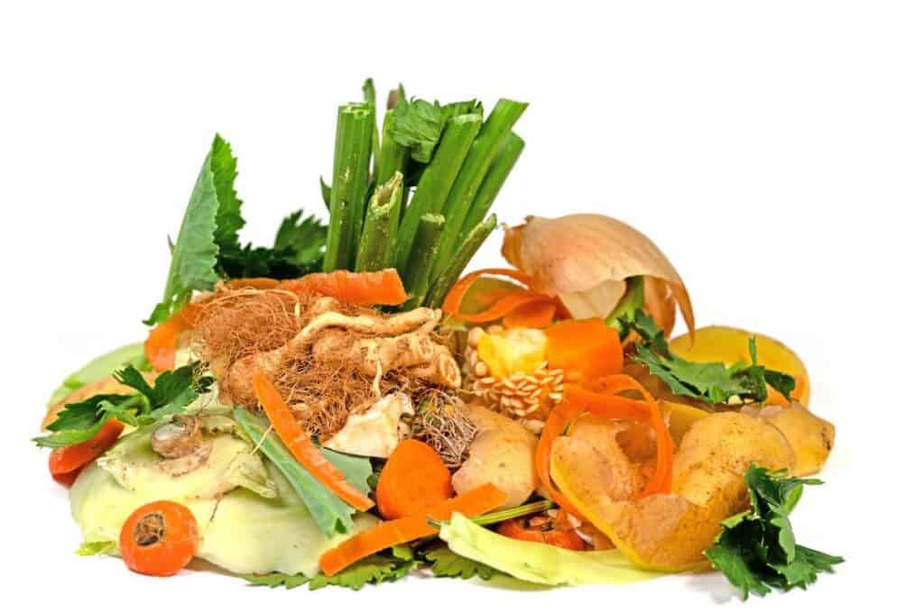 A pile of mixed vegetable scraps, perfect for a homemade vegetable broth, includes carrot peels, onion skin, celery stalks, and potato peels on a white background.