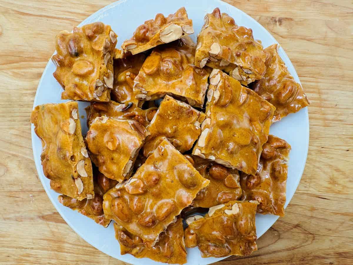 A white plate filled with pieces of peanut brittle on a wooden table.