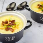 Two bowls of Copycat La Madeleine Country Potato Soup were placed on a marble surface next to two spoons.