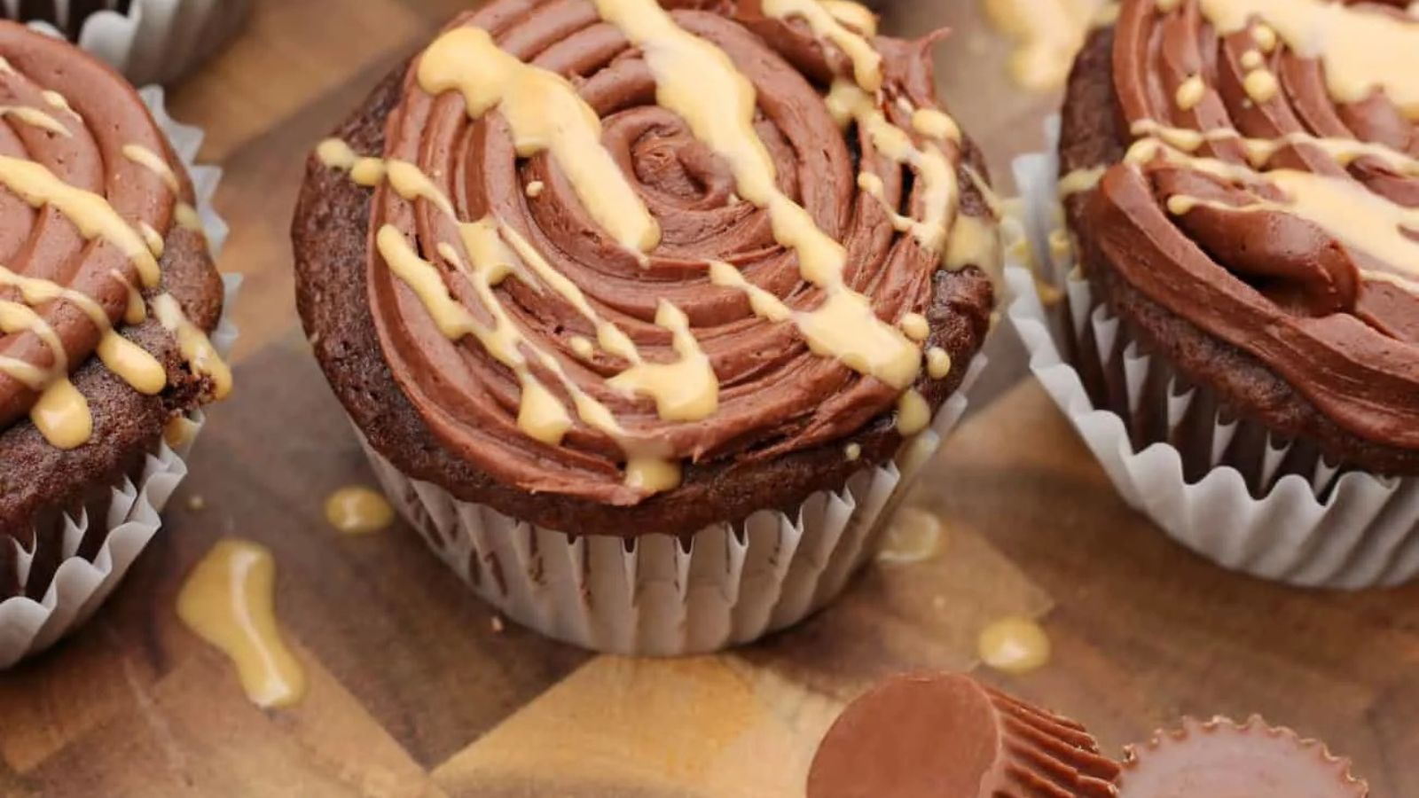 Chocolate cupcakes with swirled frosting and a drizzle of caramel sauce on top, arranged on a wooden surface.