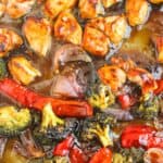 Tray of roasted chicken pieces, red peppers, broccoli, and red onions coated in a glossy sauce.