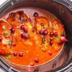 Chicken breasts in a slow cooker with red sauce, cranberries, and herbs.