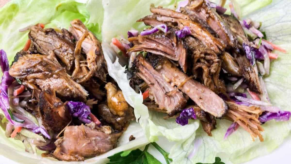 Two lettuce wraps filled with shredded meat and mixed slaw, placed on a plate.