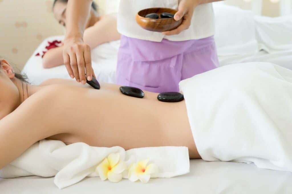 Amidst the tranquility of a wellness retreat in the Caribbean, a person enjoys a hot stone massage with delicate flowers nearby, enhancing the serene atmosphere.