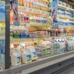 Grocery store refrigerated section filled with various dairy products and bottled water.