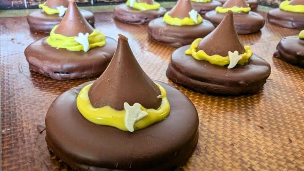 Chocolate witch hat cookies with yellow icing and white candy decorations on a baking tray.