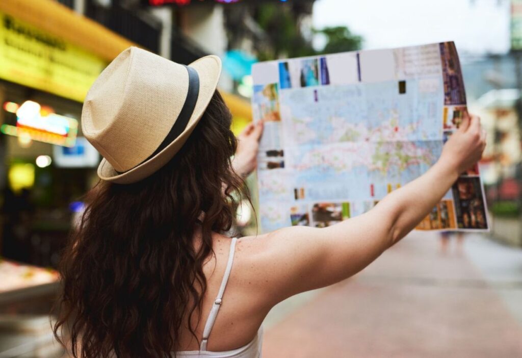 Person wearing a hat is holding and looking at a large map on a city street.