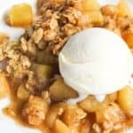 A plate of apple crisp with chunks of apple, topped with a scoop of vanilla ice cream and an oat crumble topping.