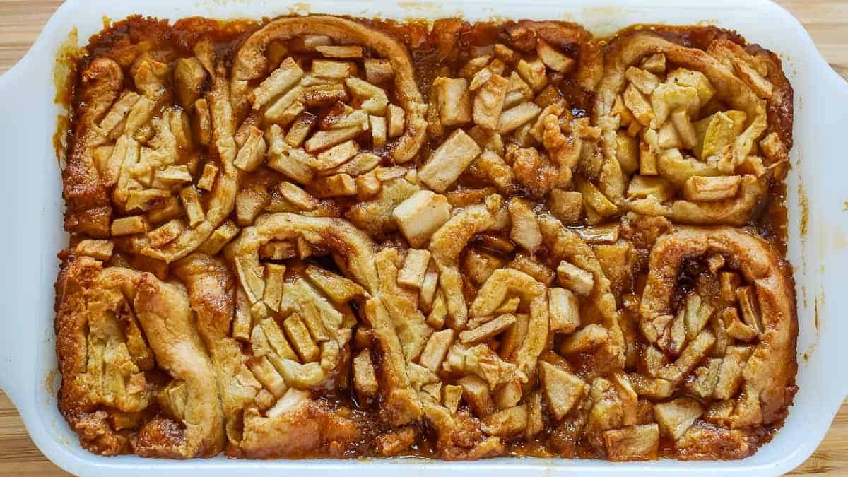 A baking dish filled with apple cinnamon rolls, topped with diced apples and a caramelized glaze.