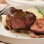 A plate with a cooked steak cut into pieces, accompanied by mashed potatoes and green beans.