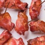 Close-up of several bacon-wrapped items secured with toothpicks, arranged on a white surface.