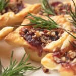 Brie bites filled with jam and chopped nuts, topped with rosemary sprigs, on a white plate.