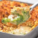 Close-up of a spoon scooping creamy broccoli casserole topped with a golden, crispy layer from a baking dish.