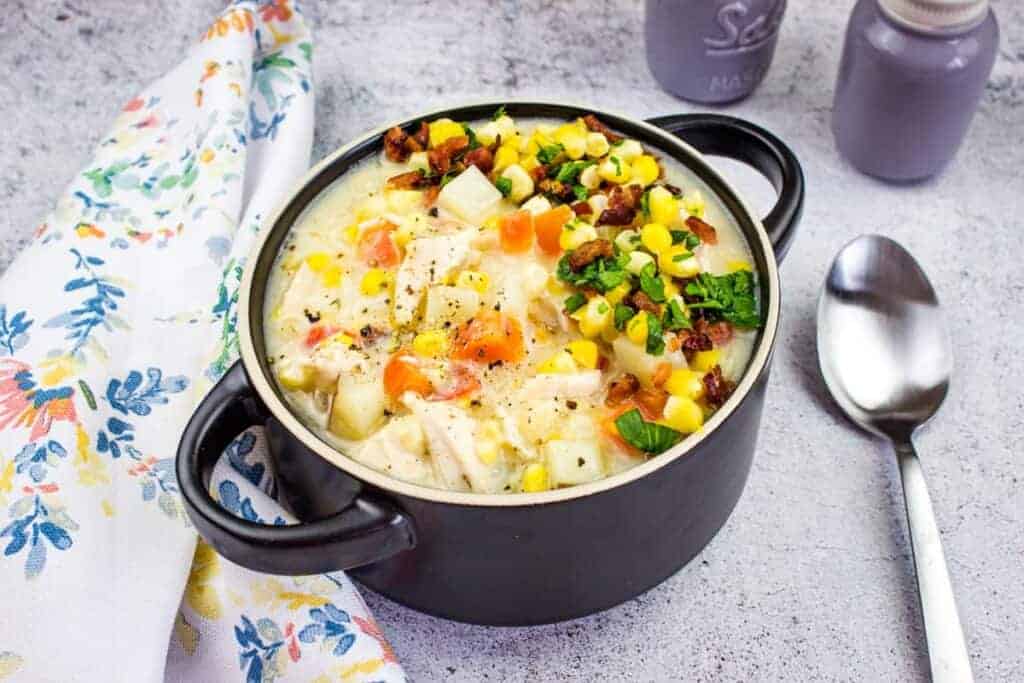 A pot of Easy Turkey And Corn Chowder next to a floral napkin and spoon.