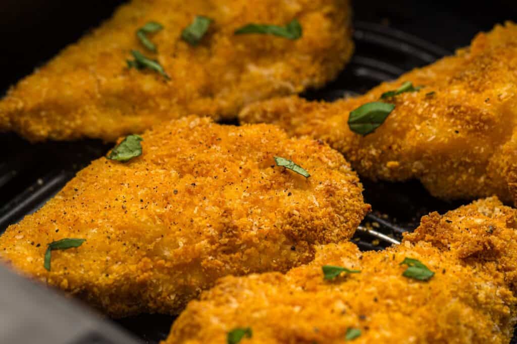 Close-up of crispy golden breaded chicken fillets garnished with chopped herbs on top.