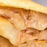 Close-up of a cheesy quesadilla with pulled chicken and melted cheese oozing between crispy, golden-brown flour tortillas.